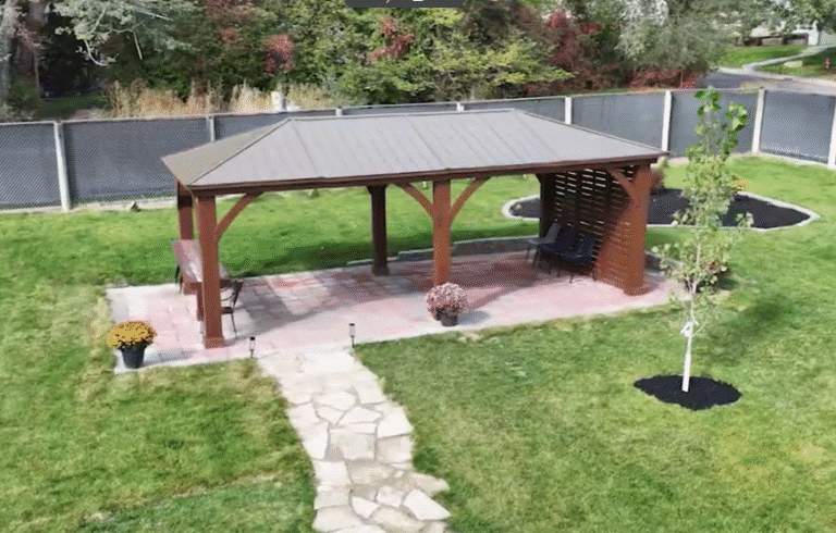 A welcoming outdoor patio area with a wooden gazebo, sitting benches, vibrant potted flowers, and landscaped greenery, providing a peaceful space for relaxation and reflection.