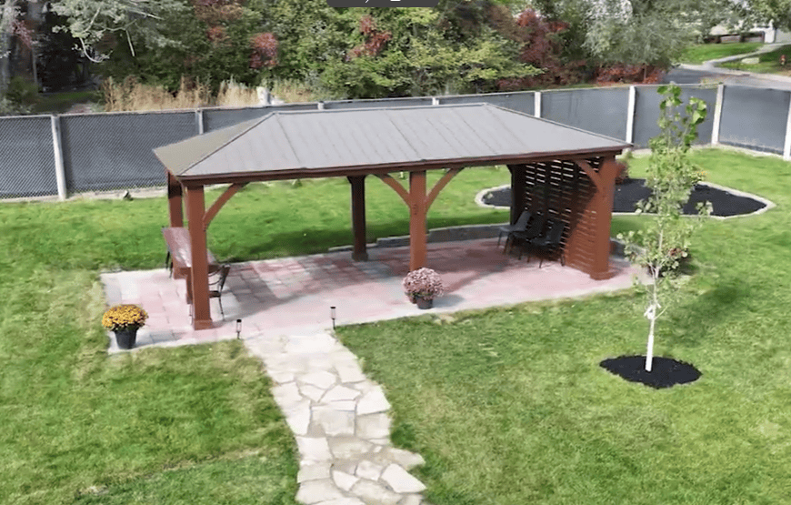 A welcoming outdoor patio area with a wooden gazebo, sitting benches, vibrant potted flowers, and landscaped greenery, providing a peaceful space for relaxation and reflection.